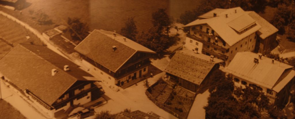 Luftaufnahme historischer Gebäude in einem Dorf, umgeben von Bäumen und kleinen Straßen.