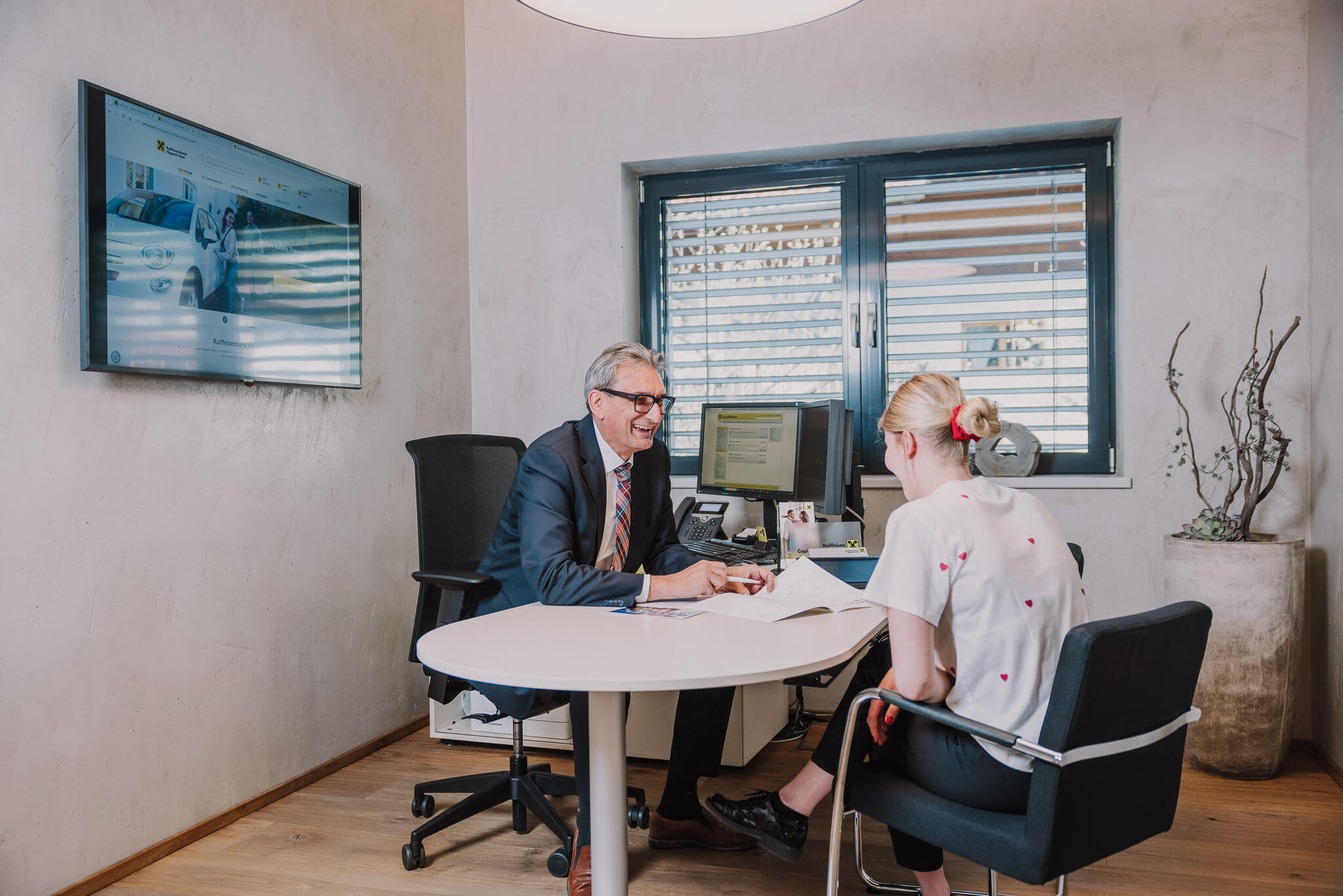 Geschäftsmann und Kundin im Beratungsgespräch im Büro, Monitor an der Wand.