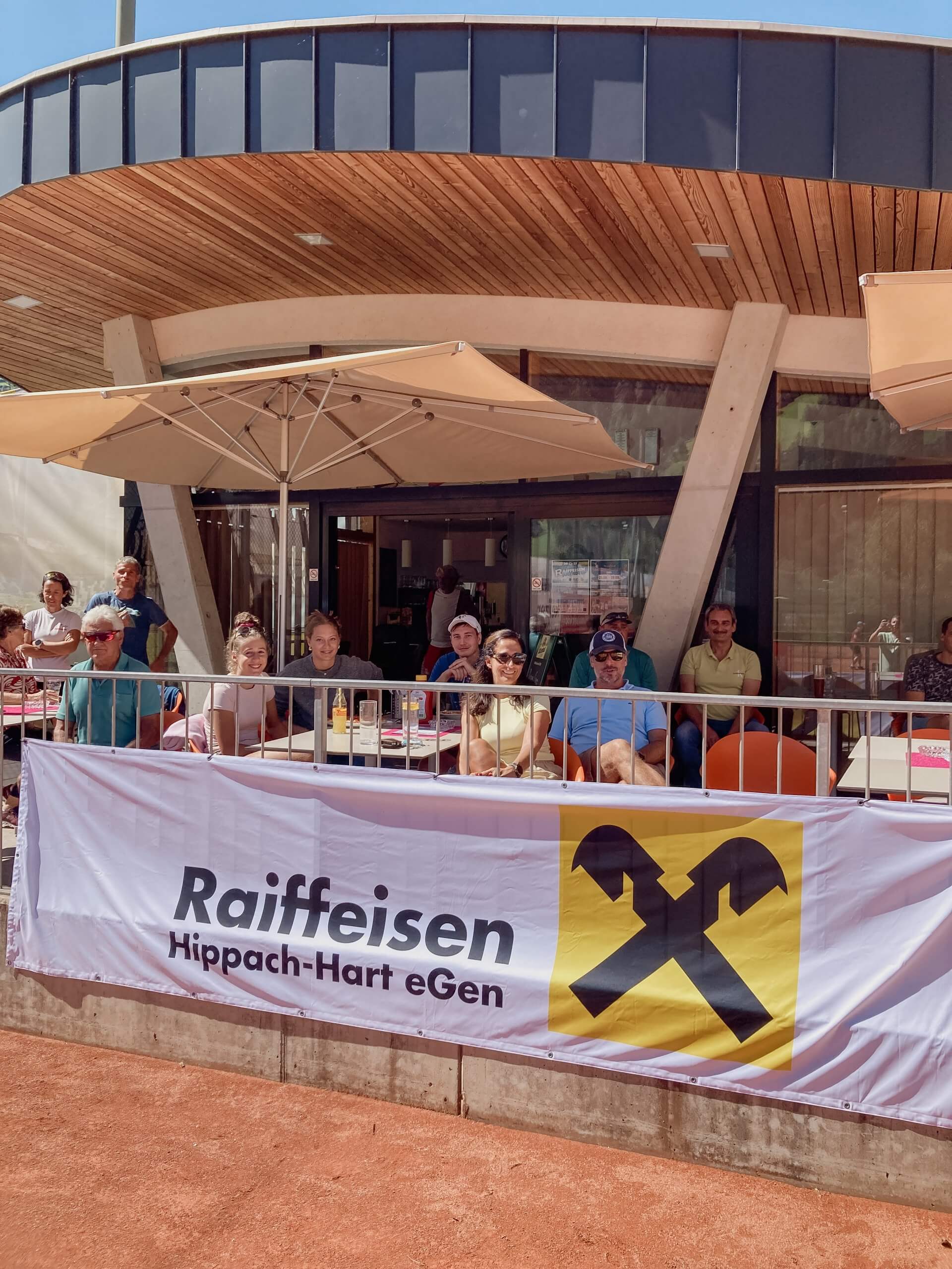 Gruppe von Menschen sitzt auf einer Terrasse mit Raiffeisen-Banner im Vordergrund.