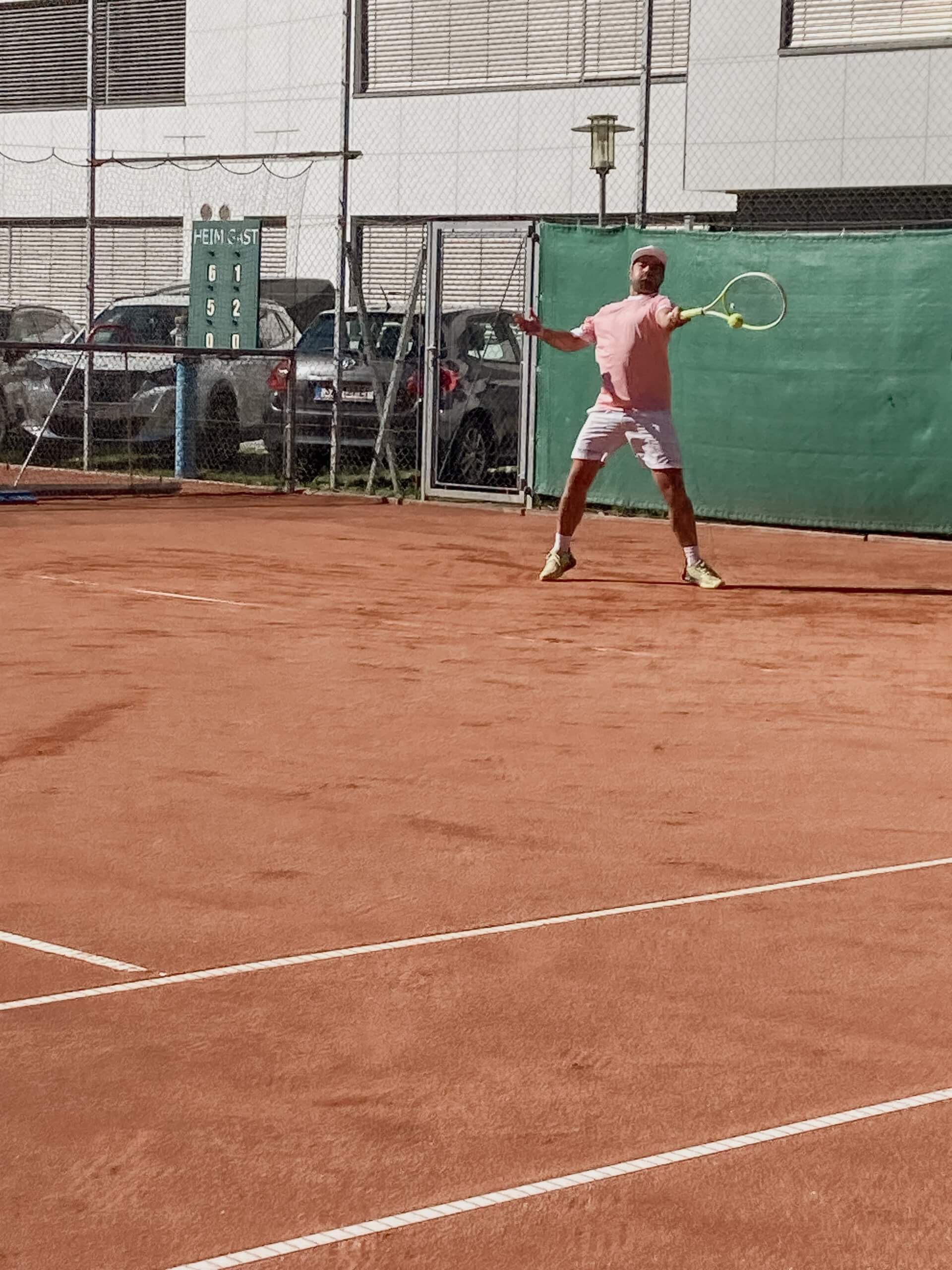 Tennisspieler auf rotem Sandplatz beim Schlag, Anzeigetafel im Hintergrund.
