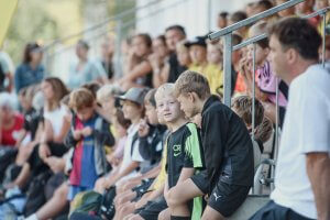 Kinder auf einer Tribüne bei einem Sportereignis, konzentriert auf das Geschehen.