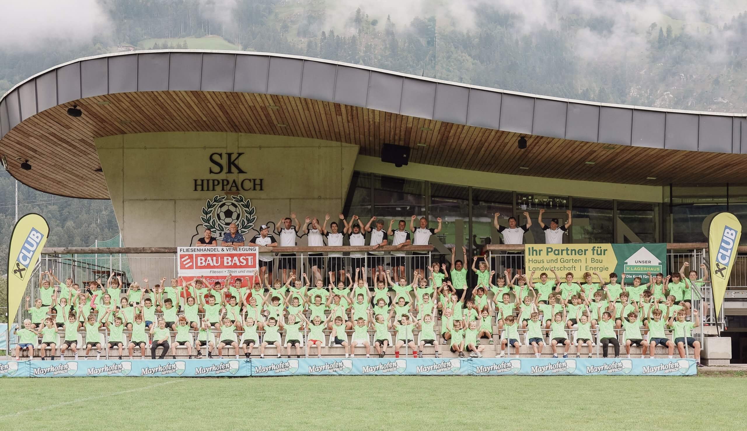 Gruppe von Kindern in grünen T-Shirts posiert vor einem Gebäude mit SK Hippach Logo.