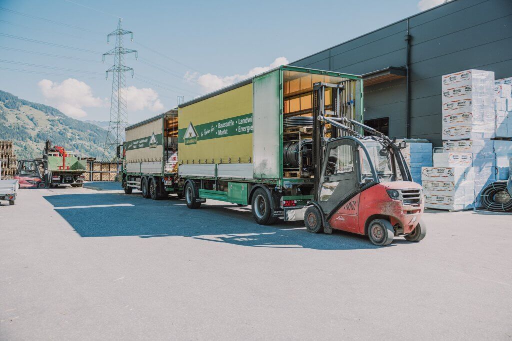 Gabelstapler lädt LKW an einem Lagerhaus vor Berglandschaft ab.