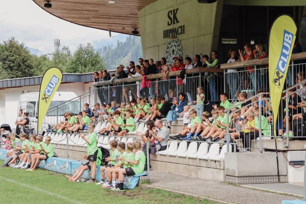 Zuschauer auf Tribüne bei Jugendfußballspiel, viele Kinder in grünen Trikots, SK Hippach Stadion.