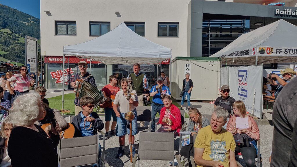 Gruppe von Menschen bei einem Outdoor-Event mit Musikern unter weißen Zelten.